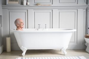 Man in his 70s enjoying a bath, relaxing in a hotel bathroom with a happy contended expression.